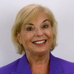 Buisness leader woman, 60 years old, blond hair, wearing a purple jacket smiling for the camera