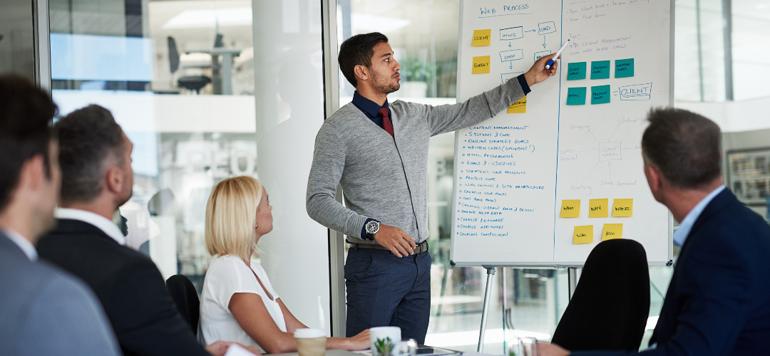 employees in focus group, one writing on white board with coloured sticky notes